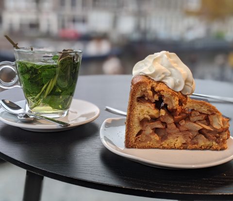 To the left there is a glass cup full of fresh mint and to the right is a huge slice of Dutch Apple Pie with a squirt of Cream on top